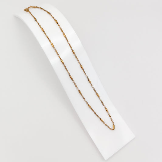 A delicate gold-plated stainless steel chain necklace featuring interspersed cylindrical bar links, displayed on a curved white presentation stand.