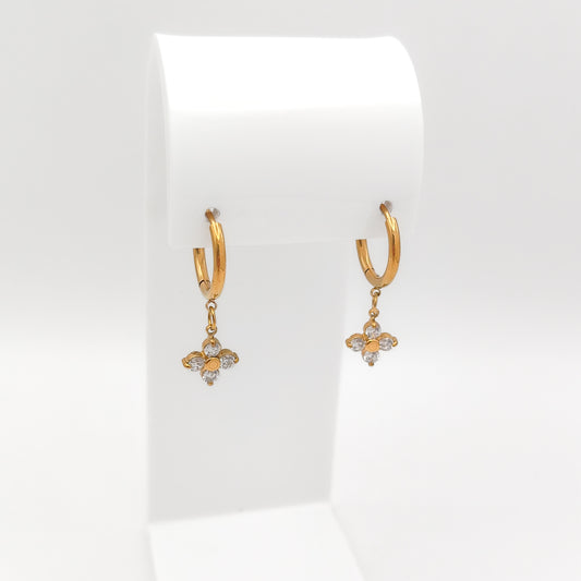 A pair of water & tarnish-resistant gold plated huggie hoop earrings with dangling floral charms, displayed on a white jewelry stand against a clean white background.