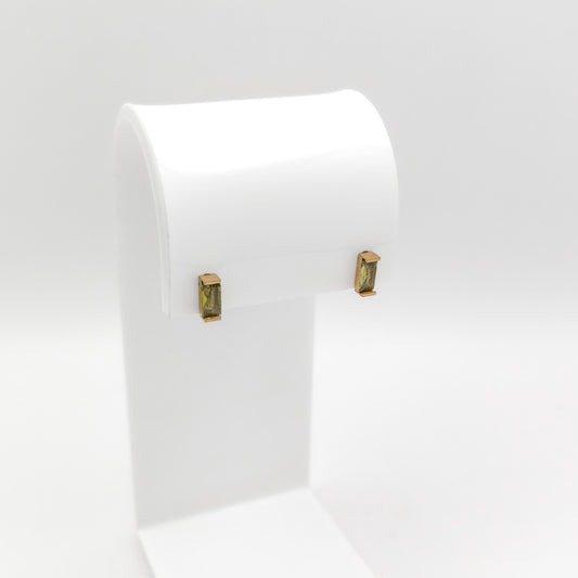 A pair of gold-toned rectangular stud earrings with green gemstone inlays, displayed on a white jewelry stand against a light gray background.