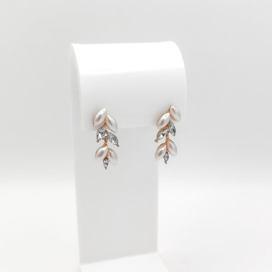 A pair of gold and rose gold leaf drop earrings with white pearls and clear marquise crystals, displayed on a white stand against a light gray background.