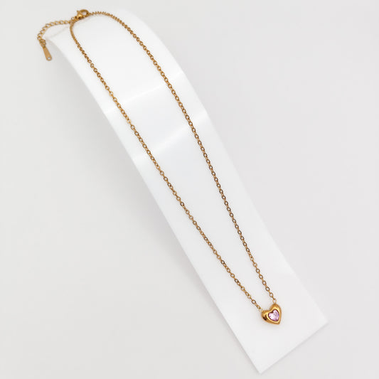 Delicate gold-plated stainless steel chain necklace with a petite heart pendant featuring a sparkling pink cubic zirconia stone, showcased on a white display stand.