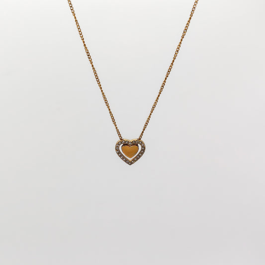 A close-up view of the gold heart-in-heart pendant, showcasing the smooth polished inner heart nestled inside a border of pavé-set clear rhinestones.
