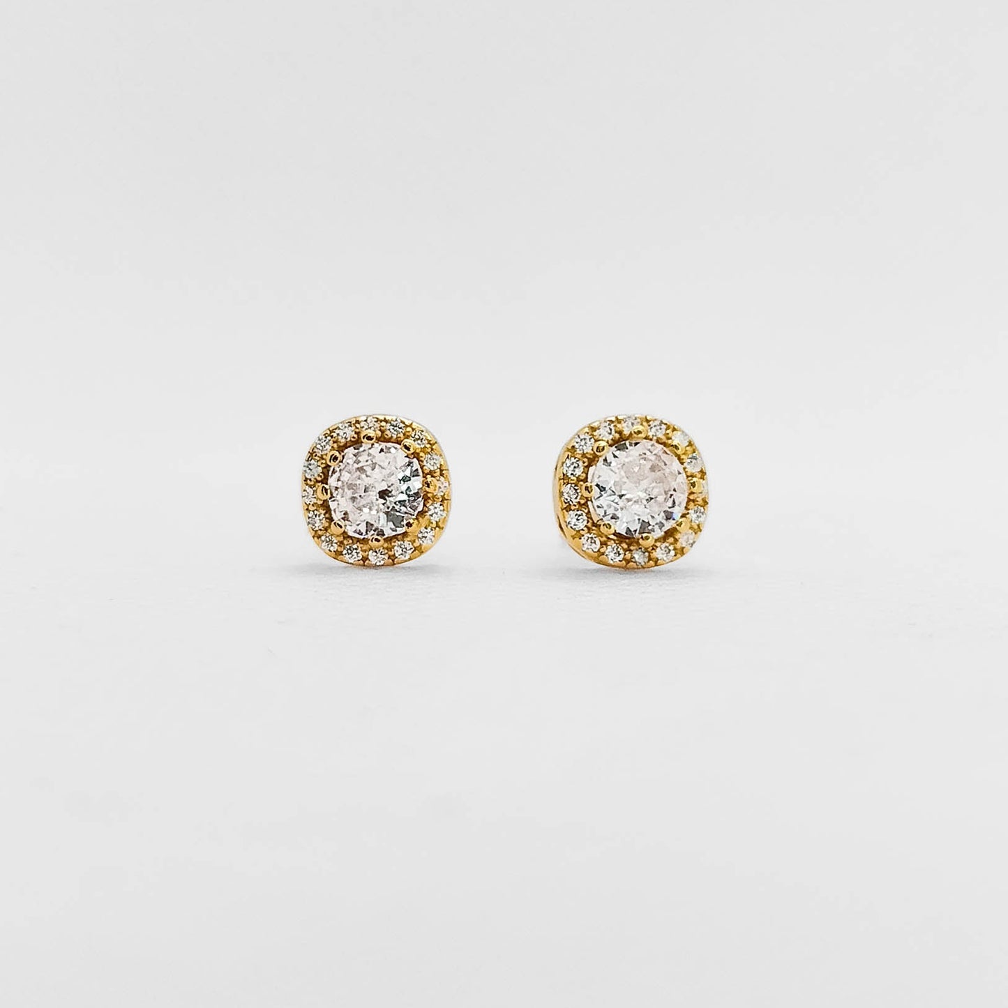 A pair of round stud earrings with clear central stones surrounded by a halo of small yellow gold stones on a plain light gray background.