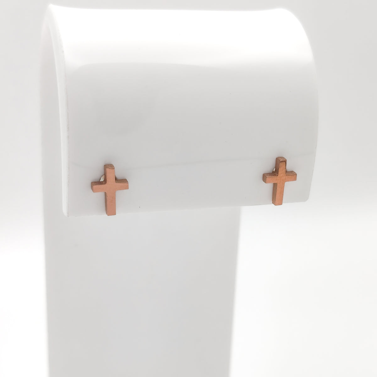 Close-up of rose gold-plated cross stud earrings showing the simple cross design.