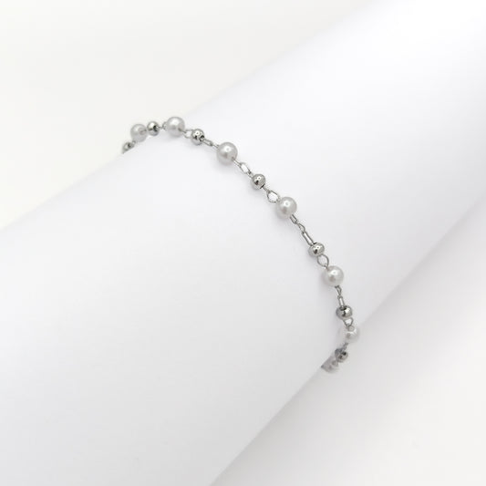 Silver-plated bracelet with white pearl beads and small silver-tone beads draped over a white display.