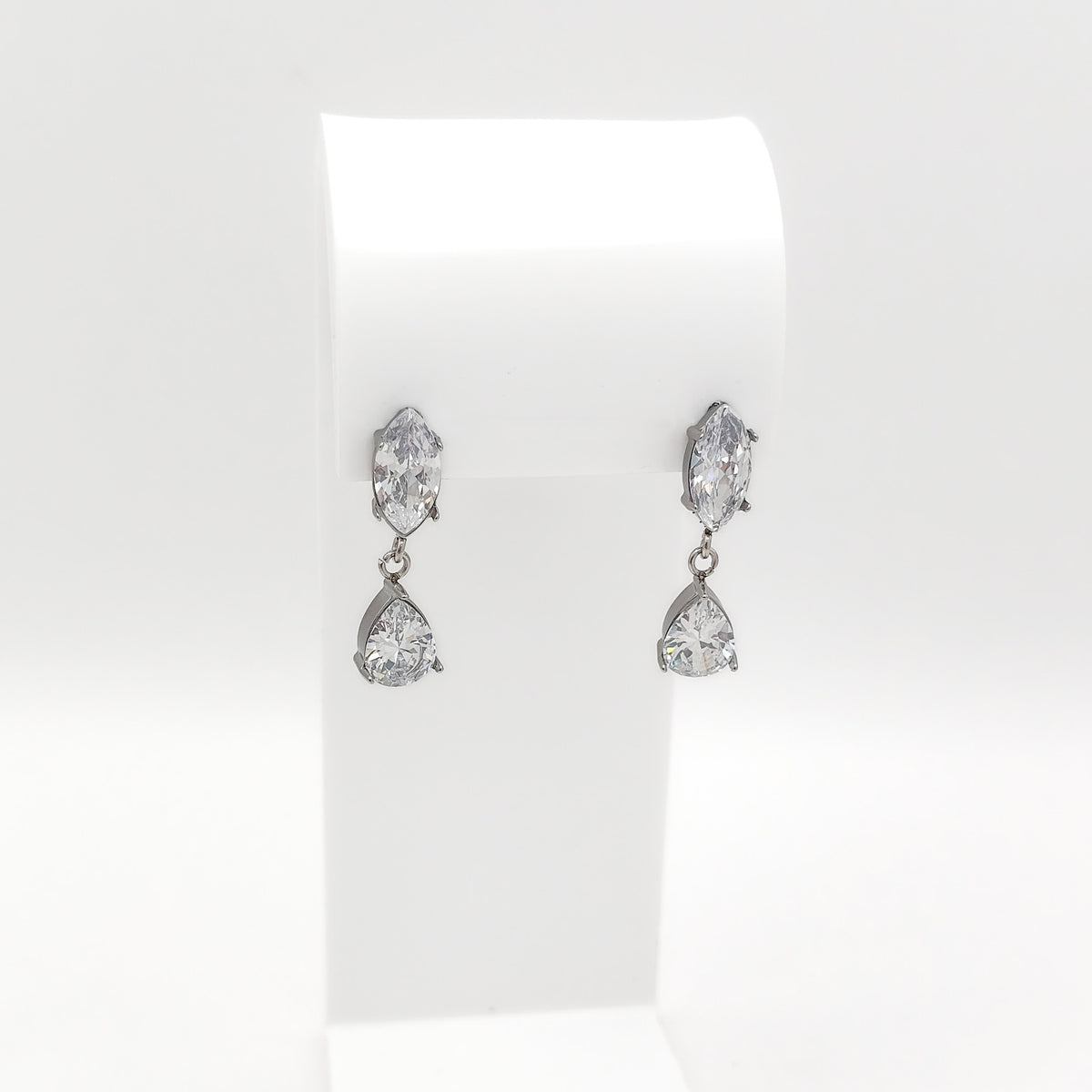 A pair of silver-tone drop earrings with marquise-cut and teardrop-cut clear gemstones, displayed on a white jewelry stand against a white background.