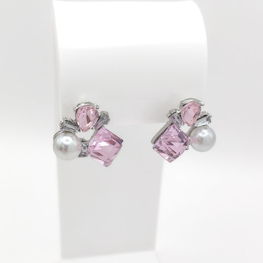 A pair of silver stud earrings with pink faceted gemstones and white faux pearls, displayed on a white jewelry stand.