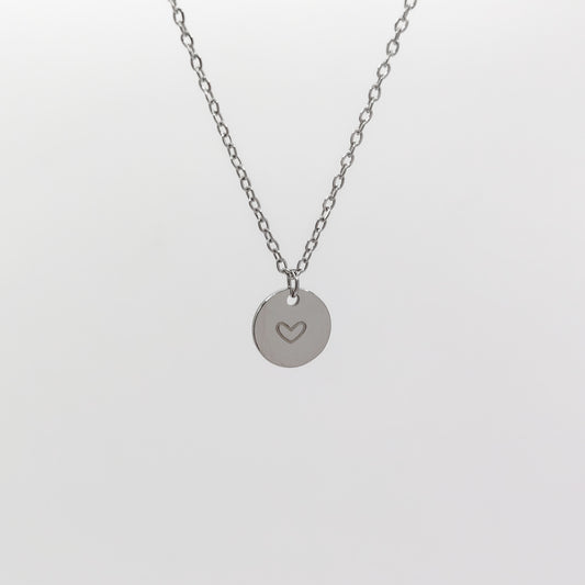 A close-up view of the stainless steel circular disc charm, showcasing the cleanly stamped heart outline and the delicate 1.5mm chain structure.