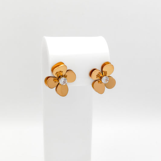 A pair of 18K gold-plated stainless steel 3D floral stud earrings featuring layered, curved heart-shaped petals and a sparkling prong-set round clear cubic zirconia center, displayed on a white stand.
