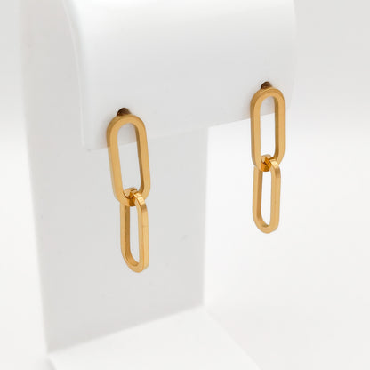 A pair of gold-toned drop earrings with elongated oval links, displayed on a white jewelry stand against a clean white background.