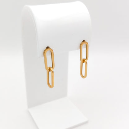 A pair of gold drop earrings with elongated oval link shapes, displayed on a white jewelry stand against a clean white background.