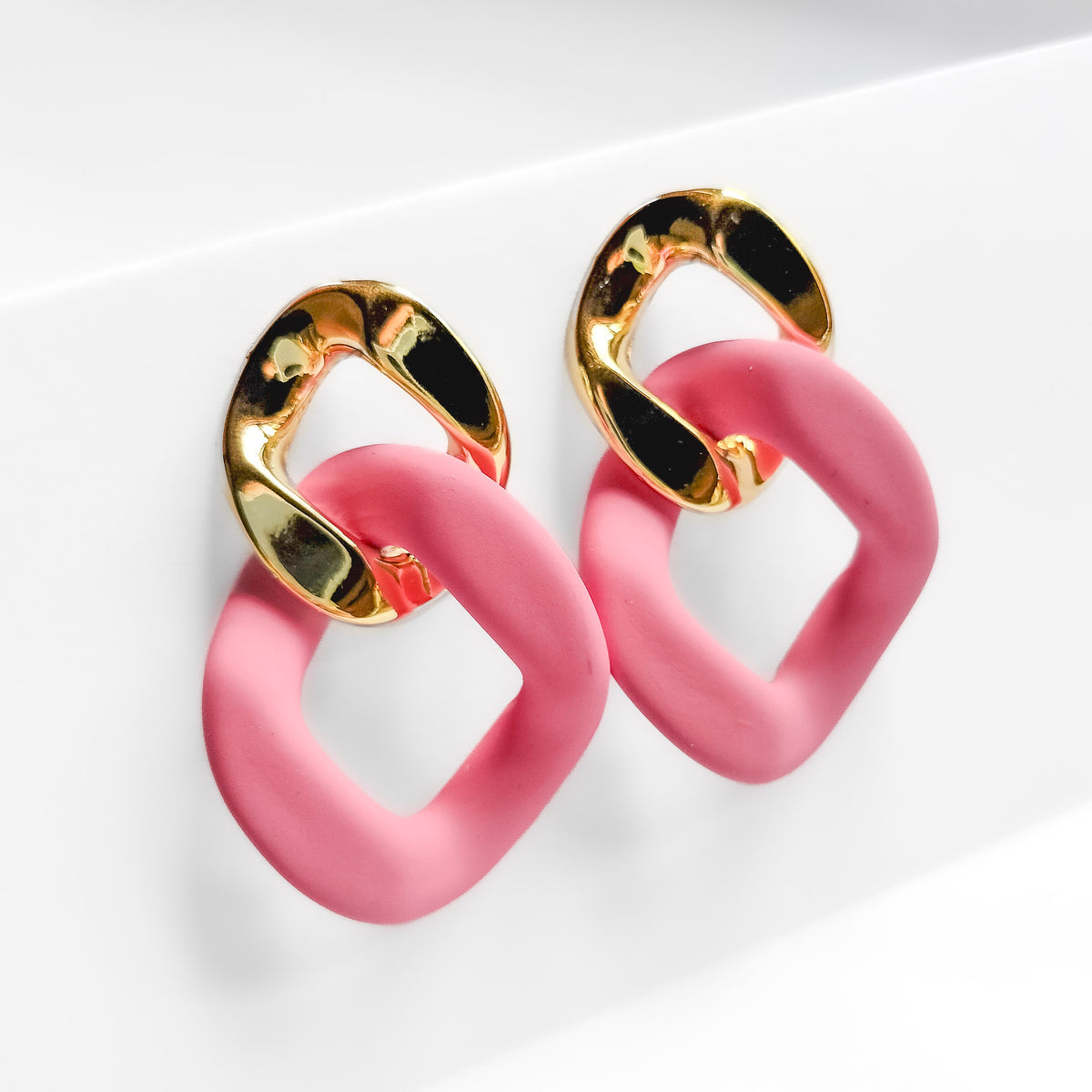 pink and gold plated chain dangle earrings on a white display