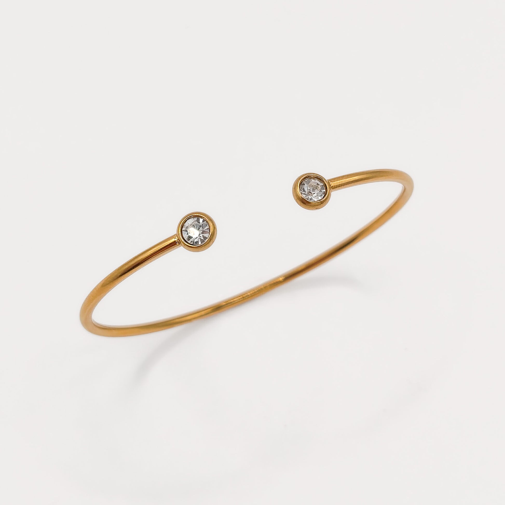 A thin gold open cuff bracelet with two small round clear gemstones set at the ends, photographed on a clean white background.