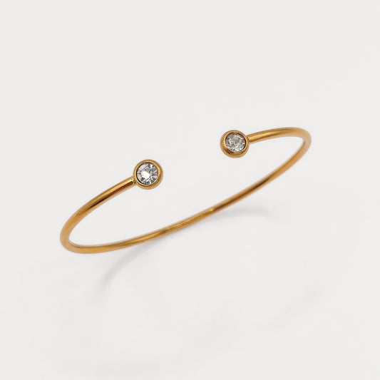 A thin gold open cuff bracelet with two small round clear gemstones set at the ends, photographed on a clean white background.