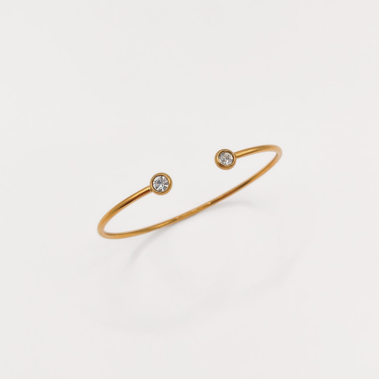 A delicate gold open cuff bracelet with two small bezel-set clear gemstones, displayed on a clean white background.