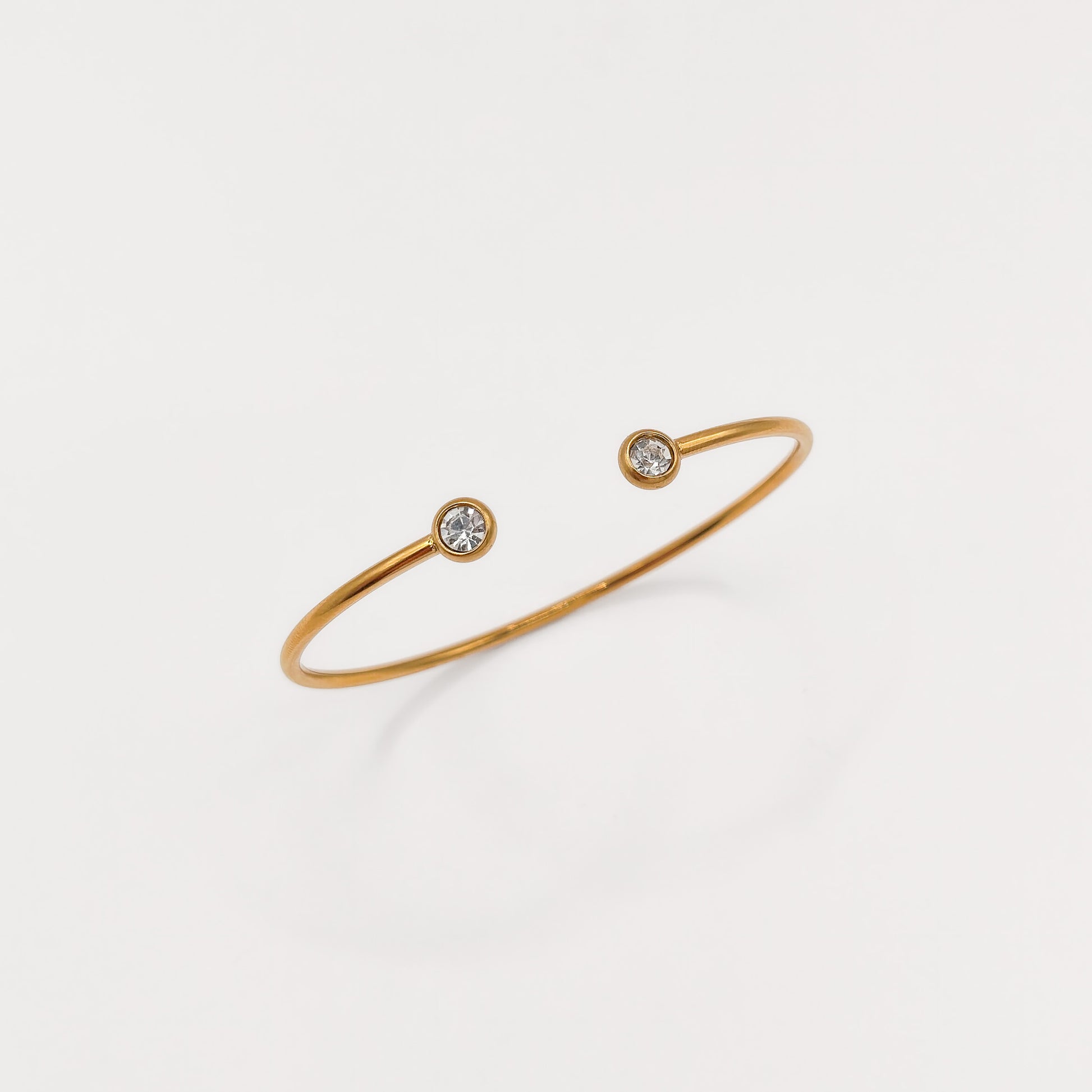 A delicate gold open cuff bracelet with two small bezel-set clear gemstones, displayed on a clean white background.