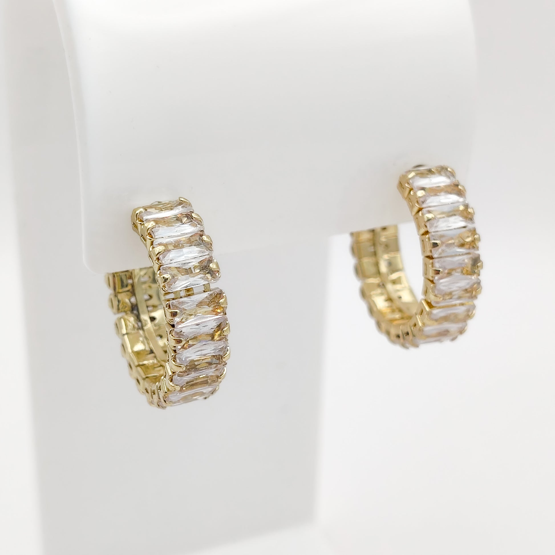 A pair of 22mm gold plated half hoop earrings set with clear baguette-cut stones, displayed on a white jewelry stand against a white background.
