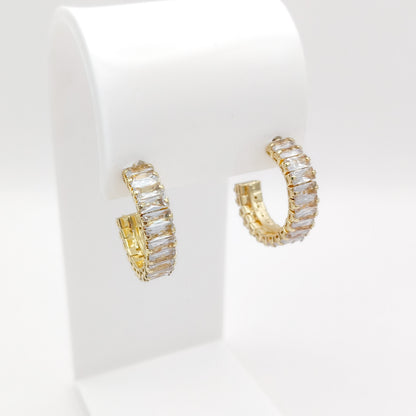 A pair of 25mm gold plated hoop earrings with rectangular clear stones, displayed on a white jewelry stand against a white background.