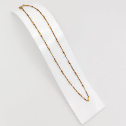 A delicate gold-plated stainless steel chain necklace featuring interspersed cylindrical bar links, displayed on a curved white presentation stand.