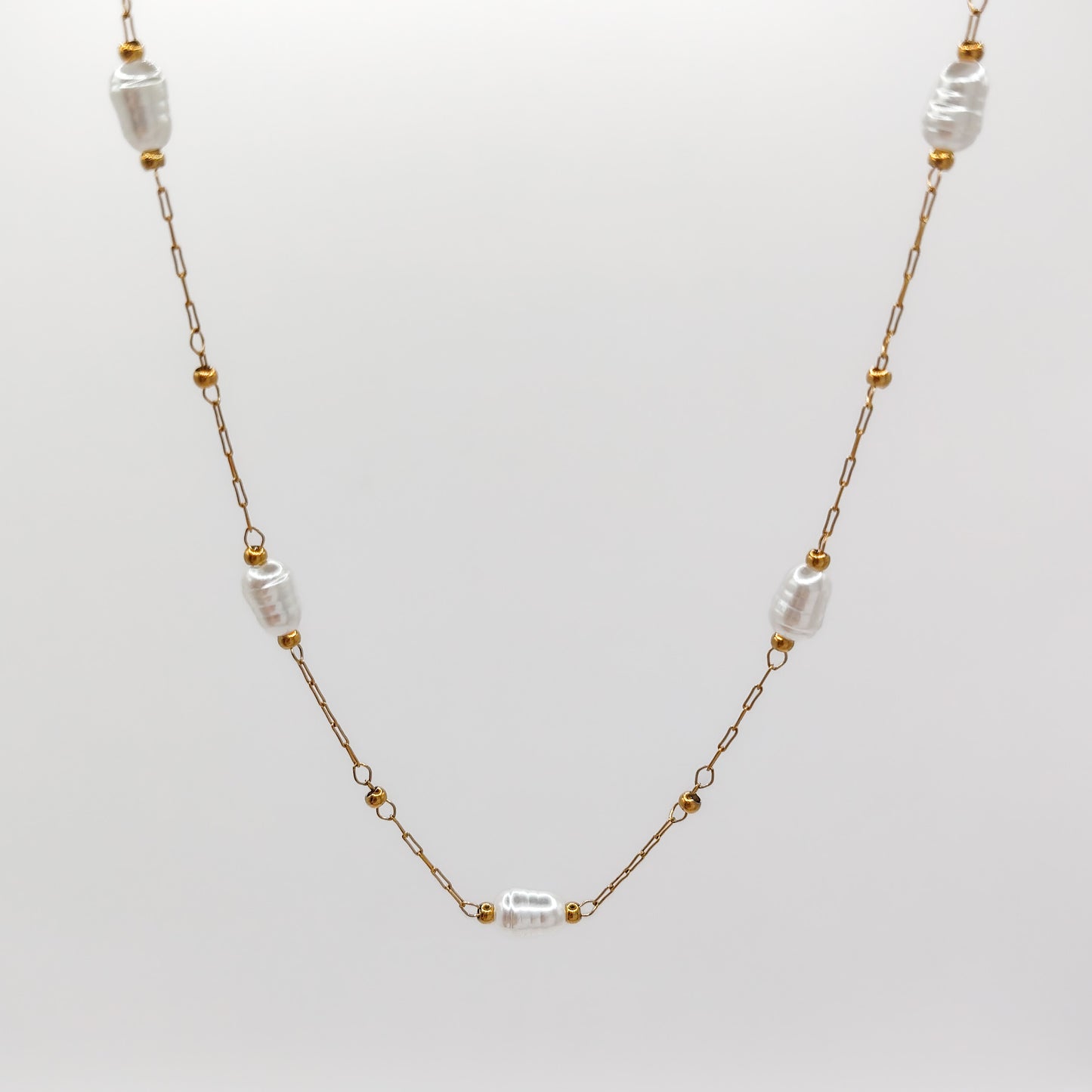 Close-up view of the fine gold-plated link chain, highlighting the smooth, organic luster of the imitation station pearls framed by small golden accent beads.