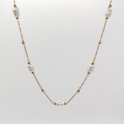 Close-up view of the fine gold-plated link chain, highlighting the smooth, organic luster of the imitation station pearls framed by small golden accent beads.