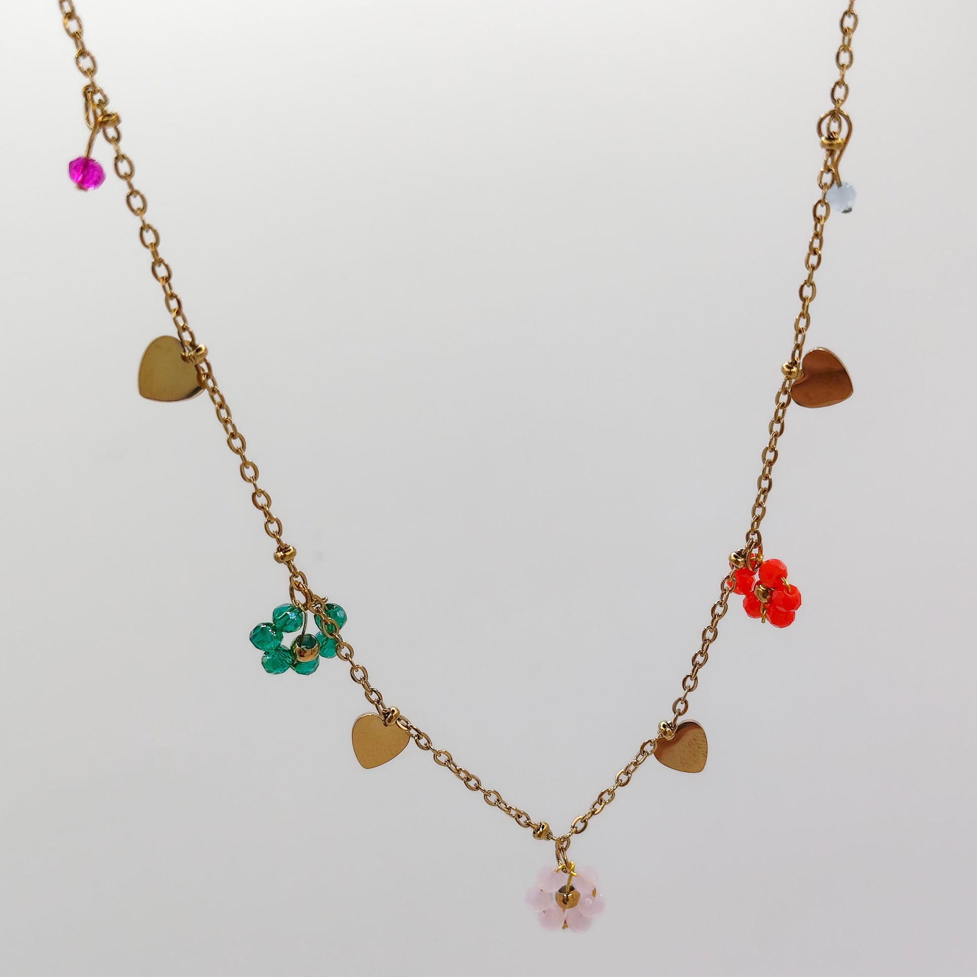 A close-up view of the gold charm necklace detailing the vibrant green, red, and pale pink beaded flowers alongside polished gold dangling hearts.