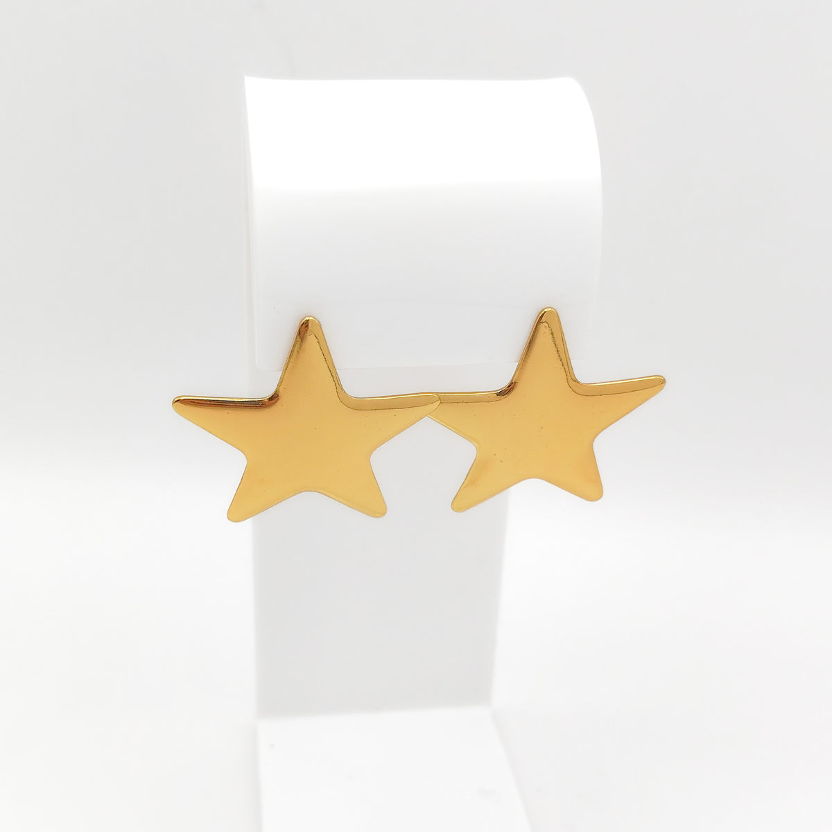 Pair of high-polish gold-plated stainless steel star stud earrings displayed on a white stand.