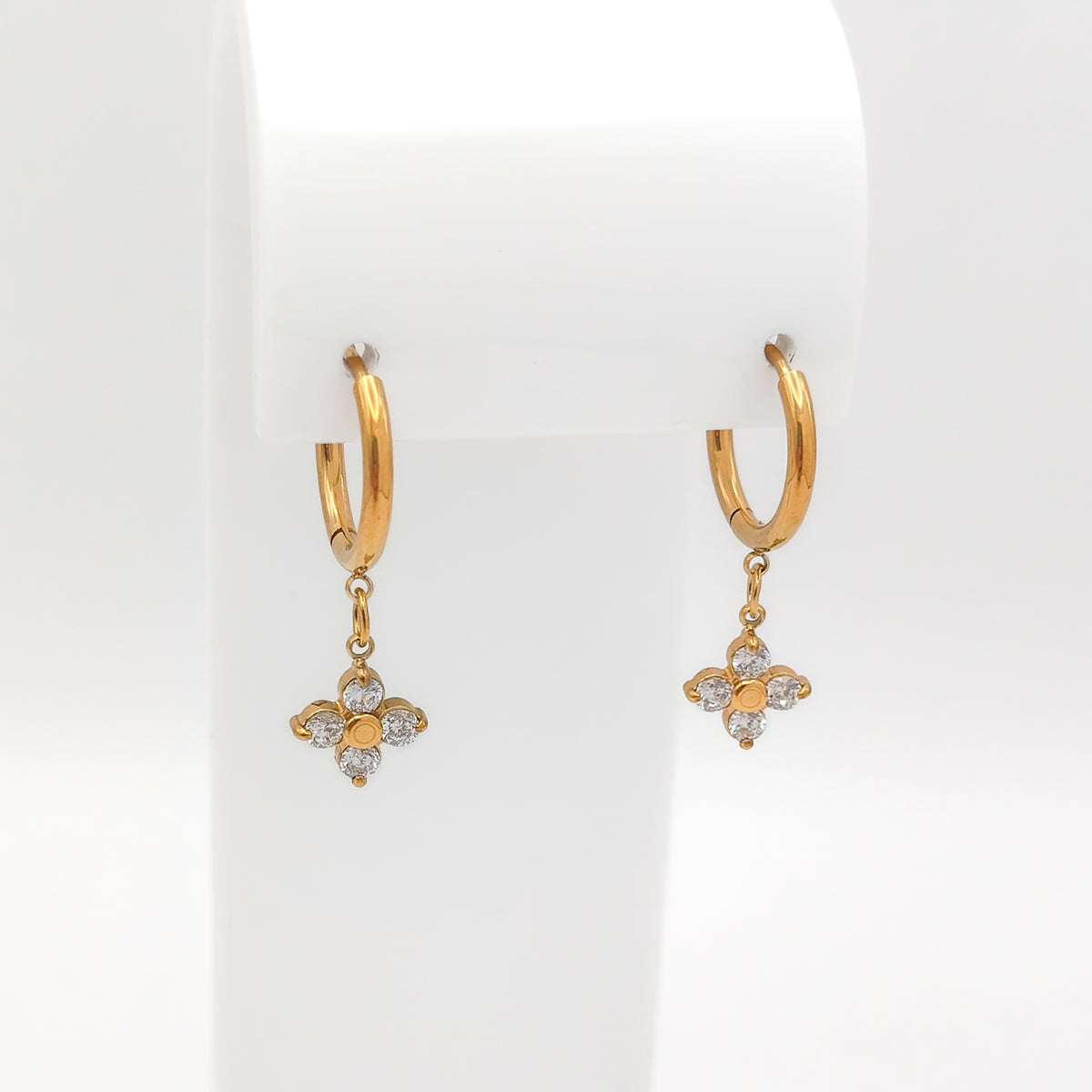 A pair of water & tarnish-resistant gold plated hoop earrings with dangling floral clover charms, displayed on a white jewelry stand against a white background.