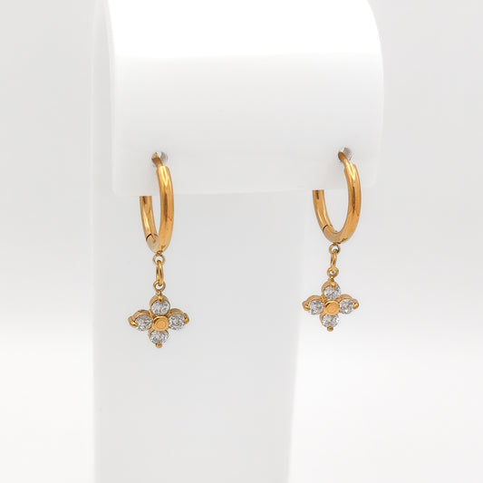 A pair of water & tarnish-resistant gold plated hoop earrings with dangling floral clover charms, displayed on a white jewelry stand against a white background.