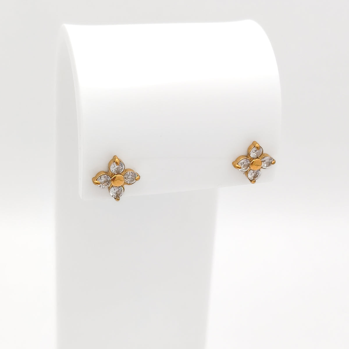 A pair of water & tarnish-resistant gold plated flower-shaped stud earrings with clear gemstones, displayed on a white jewelry stand against a white background.