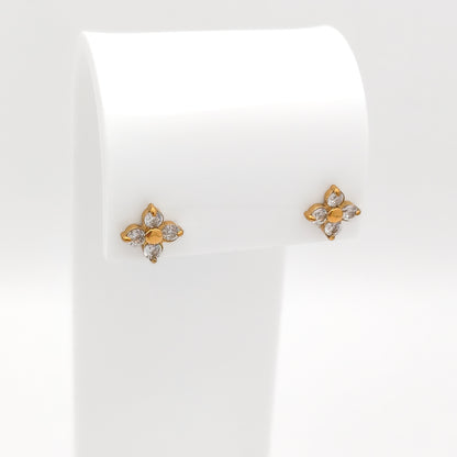 A pair of water & tarnish-resistant gold plated flower-shaped stud earrings with clear gemstones, displayed on a white jewelry stand against a white background.