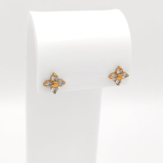 A pair of water & tarnish-resistant gold plated flower-shaped stud earrings with clear gemstones, displayed on a white jewelry stand against a white background.