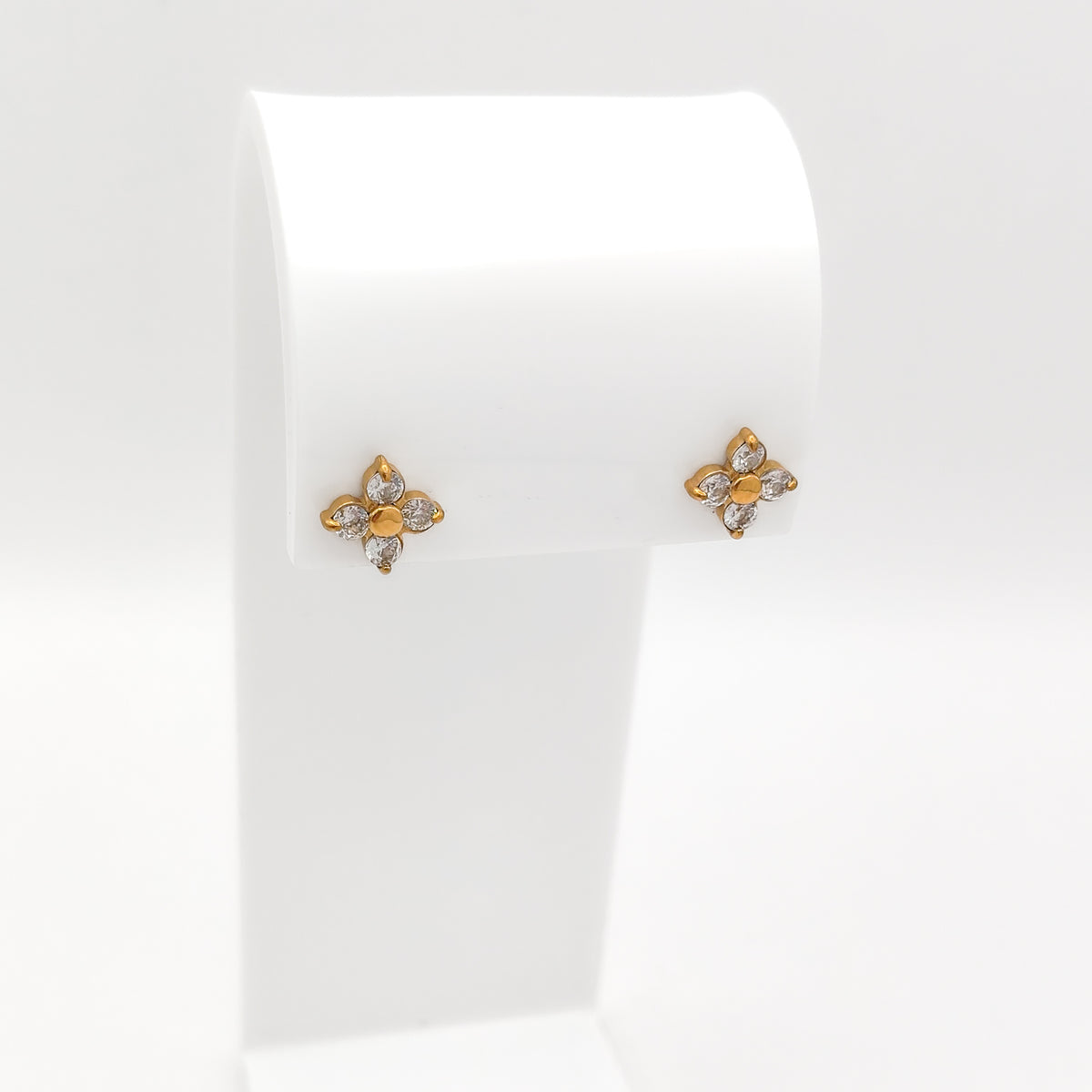 A pair of small water & tarnish-resistant gold plated flower-shaped stud earrings with clear stones, displayed on a white jewelry stand against a white background.