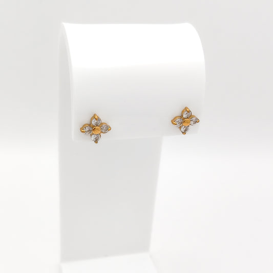 A pair of small water & tarnish-resistant gold plated flower-shaped stud earrings with clear stones, displayed on a white jewelry stand against a white background.
