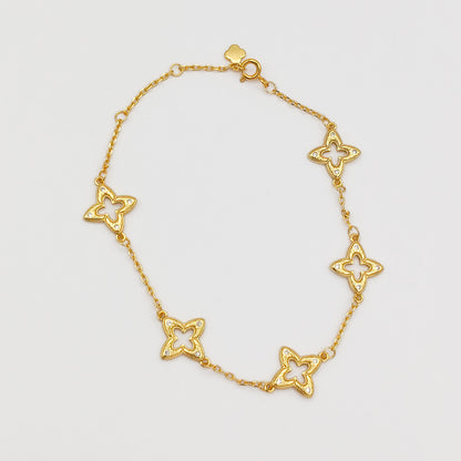 Full view of the gold-plated charm bracelet laid flat, showing five cutout filigree clover links, a spring-ring clasp, and a small flower charm tag.