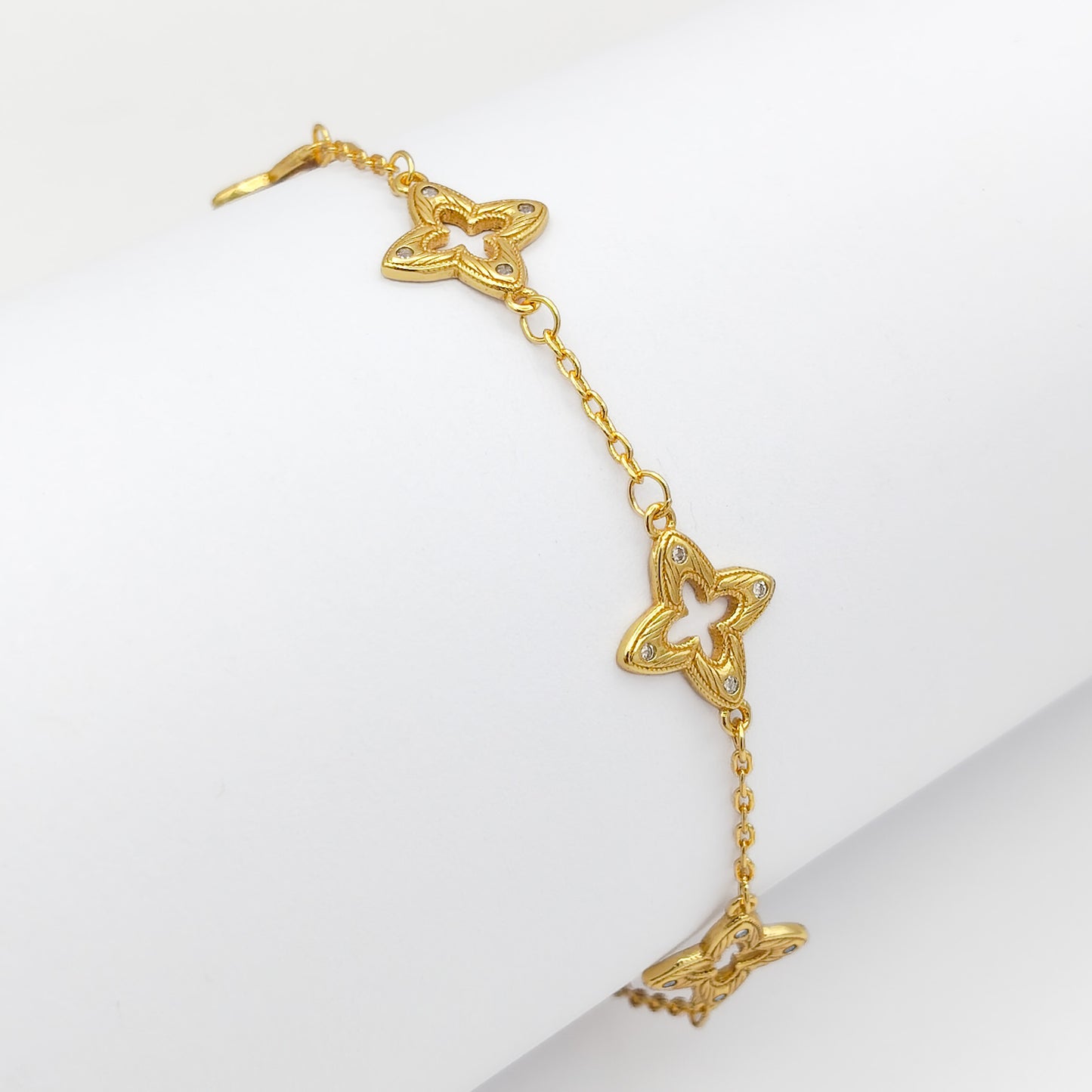A gold-plated copper chain bracelet featuring intricate filigree clover charms with clear rhinestone accents, draped over a white display.