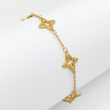 A gold-plated copper chain bracelet featuring intricate filigree clover charms with clear rhinestone accents, draped over a white display.