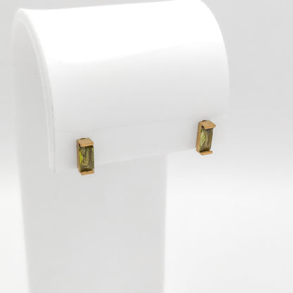 A pair of gold post earrings with rectangular green gemstones, displayed on a white jewelry stand against a white background.