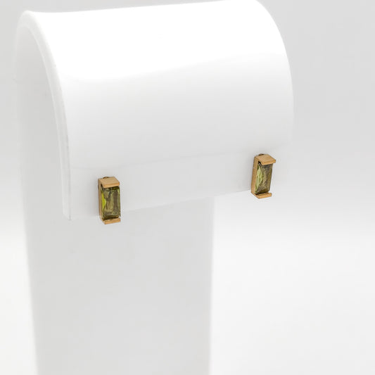 A pair of gold post earrings with rectangular green gemstones, displayed on a white jewelry stand against a white background.