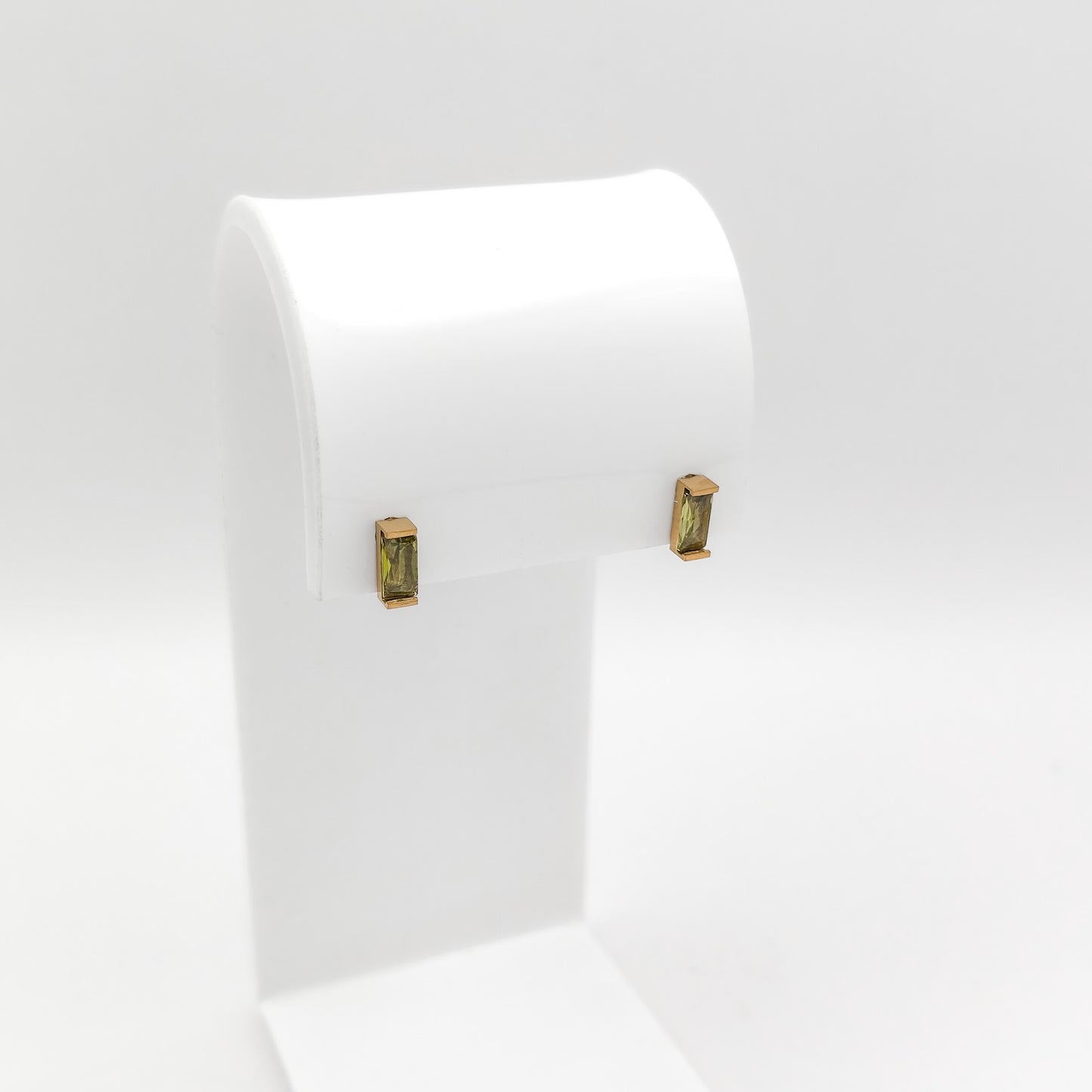 A pair of gold-toned rectangular stud earrings with green gemstone inlays, displayed on a white jewelry stand against a light gray background.