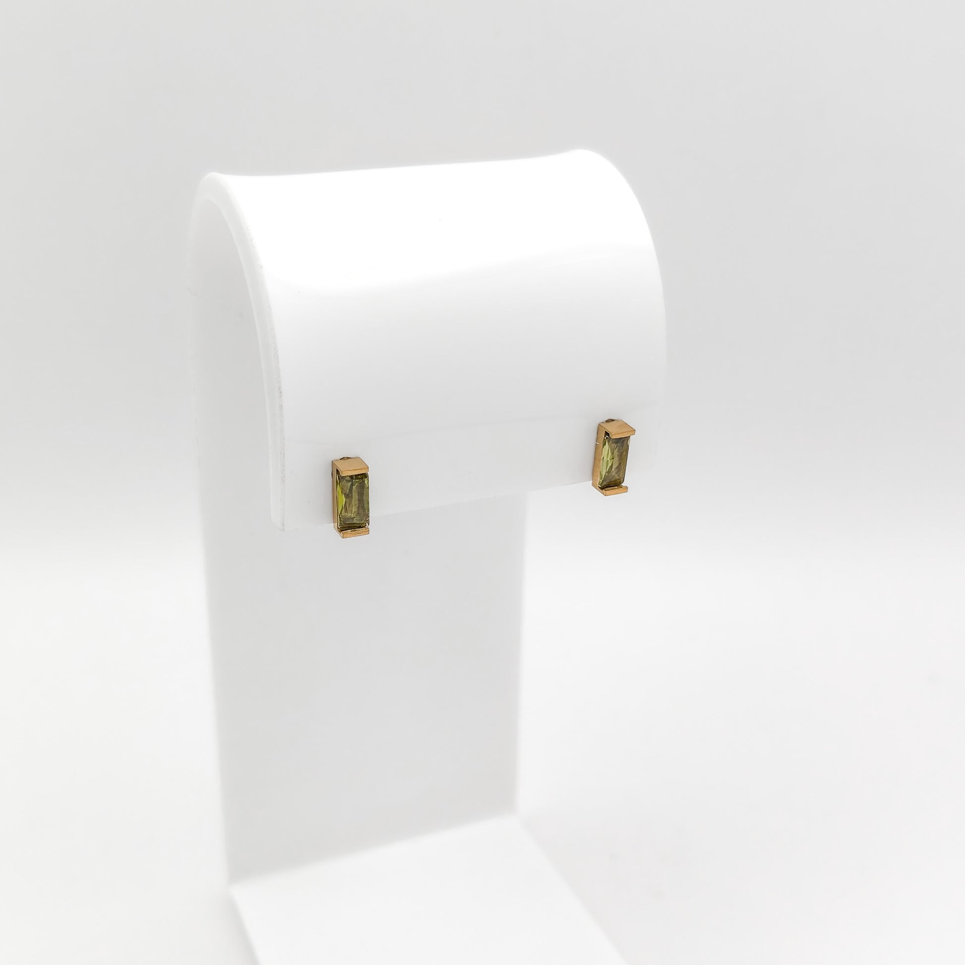 A pair of gold-toned rectangular stud earrings with green gemstone inlays, displayed on a white jewelry stand against a light gray background.