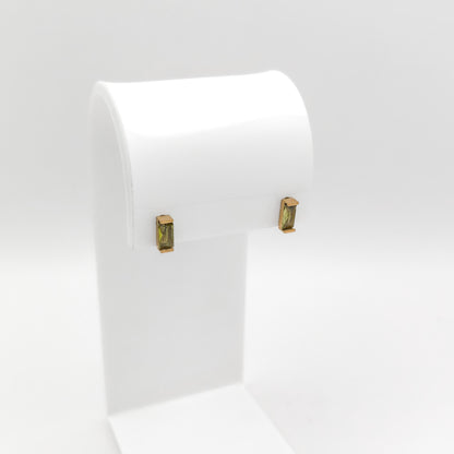 A pair of gold-toned rectangular stud earrings with green gemstone inlays, displayed on a white jewelry stand against a light gray background.