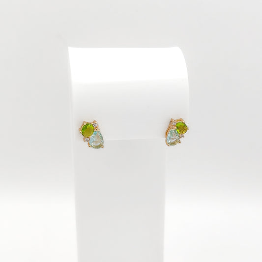A pair of gold stud earrings with green and iridescent blue-green gemstones, displayed on a white jewelry stand against a white background.