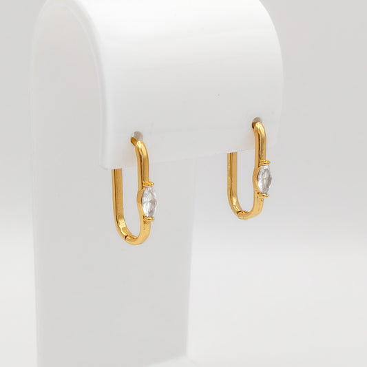 A pair of gold plated marquise CZ oval huggie earrings featuring a single bezel-set marquise-cut clear cubic zirconia stone on the front, displayed on a white stand.