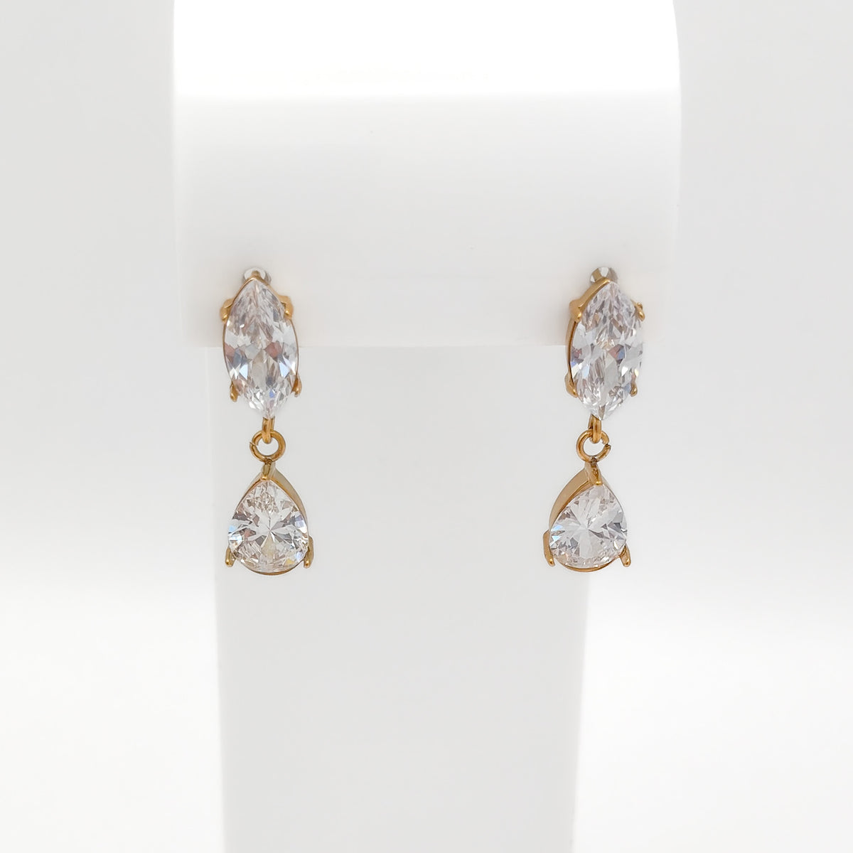 A pair of gold drop earrings with marquise-cut clear crystals on the top and pear-cut clear crystals below, displayed on a white jewelry stand.
