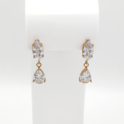 A pair of gold drop earrings with marquise-cut clear crystals on the top and pear-cut clear crystals below, displayed on a white jewelry stand.