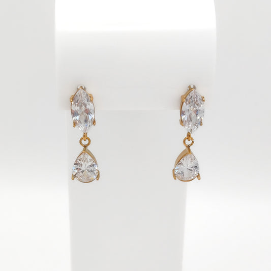 A pair of gold drop earrings with marquise-cut clear crystals on the top and pear-cut clear crystals below, displayed on a white jewelry stand.
