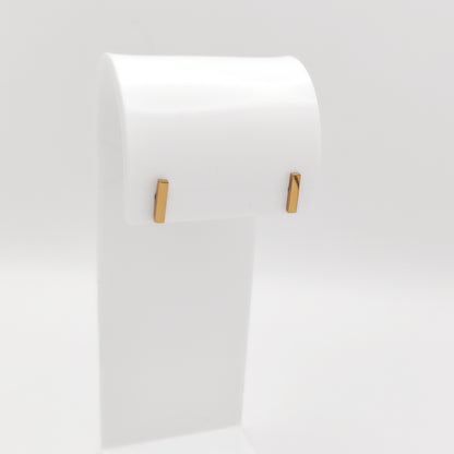 A pair of gold-plated stainless steel minimalist vertical bar stud earrings with a high-shine polished finish, displayed on a white stand.