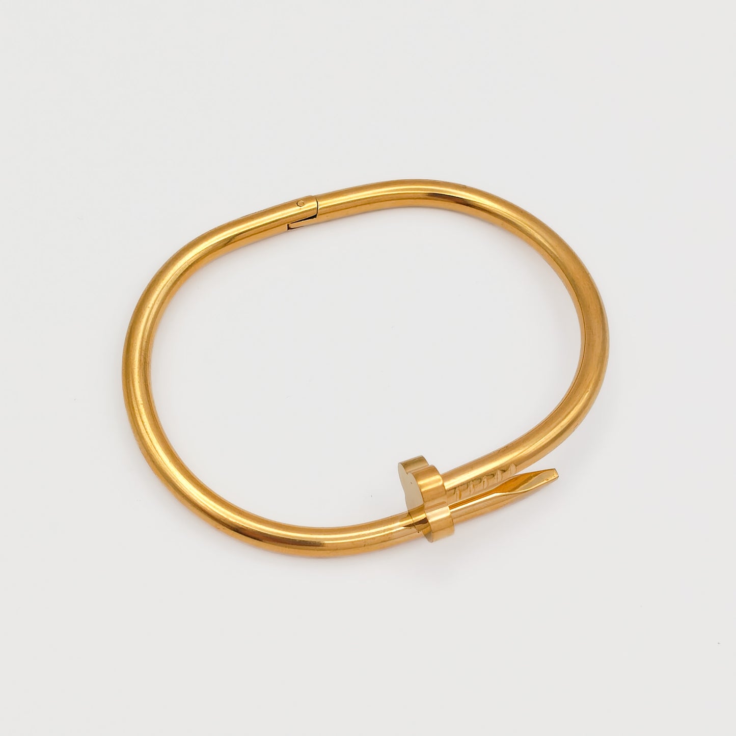 Flat lay view of the closed gold plated nail hinge bangle, showcasing its precise 6.0cm oval contour and tarnish-free stainless steel design.