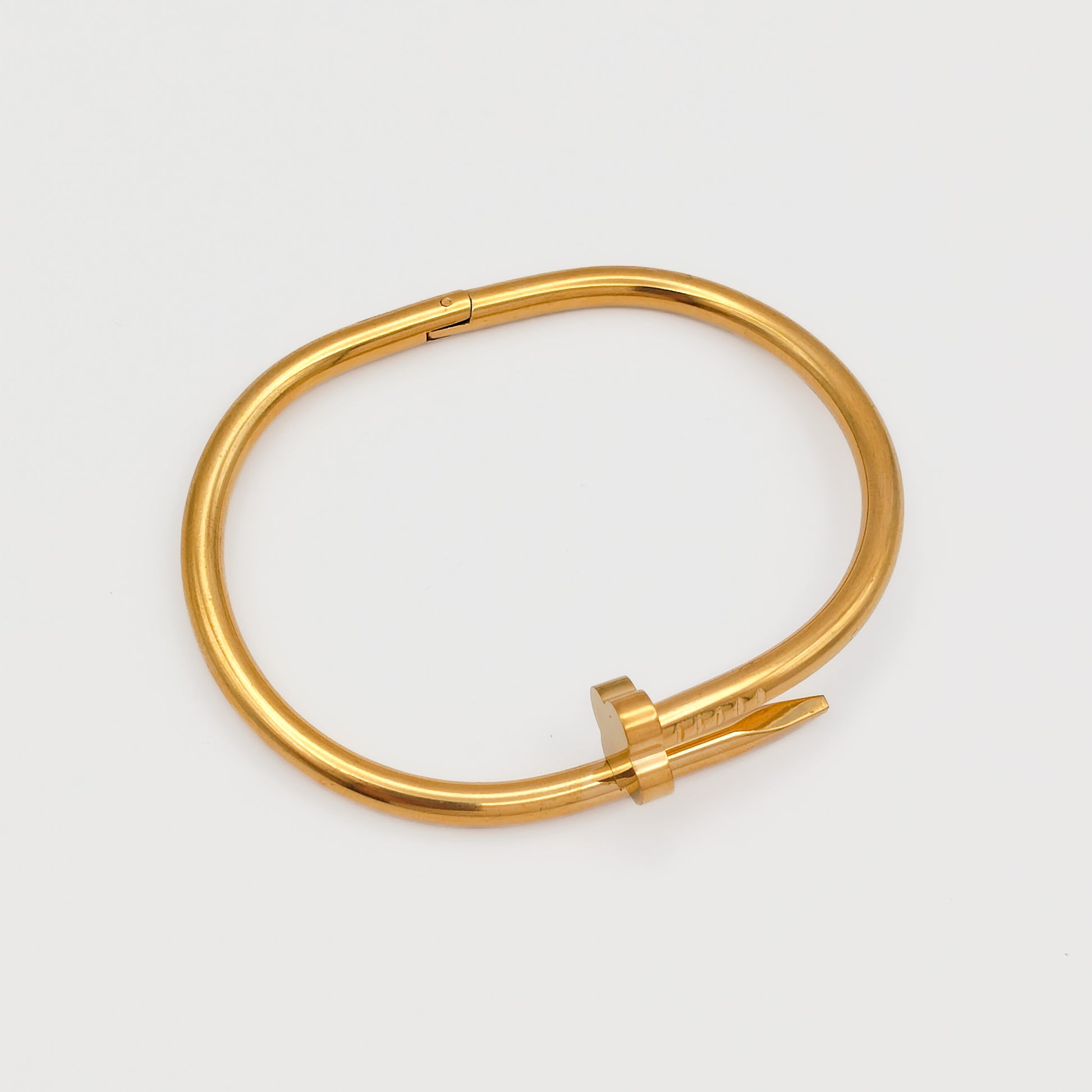Flat lay view of the closed gold plated nail hinge bangle, showcasing its precise 6.0cm oval contour and tarnish-free stainless steel design.